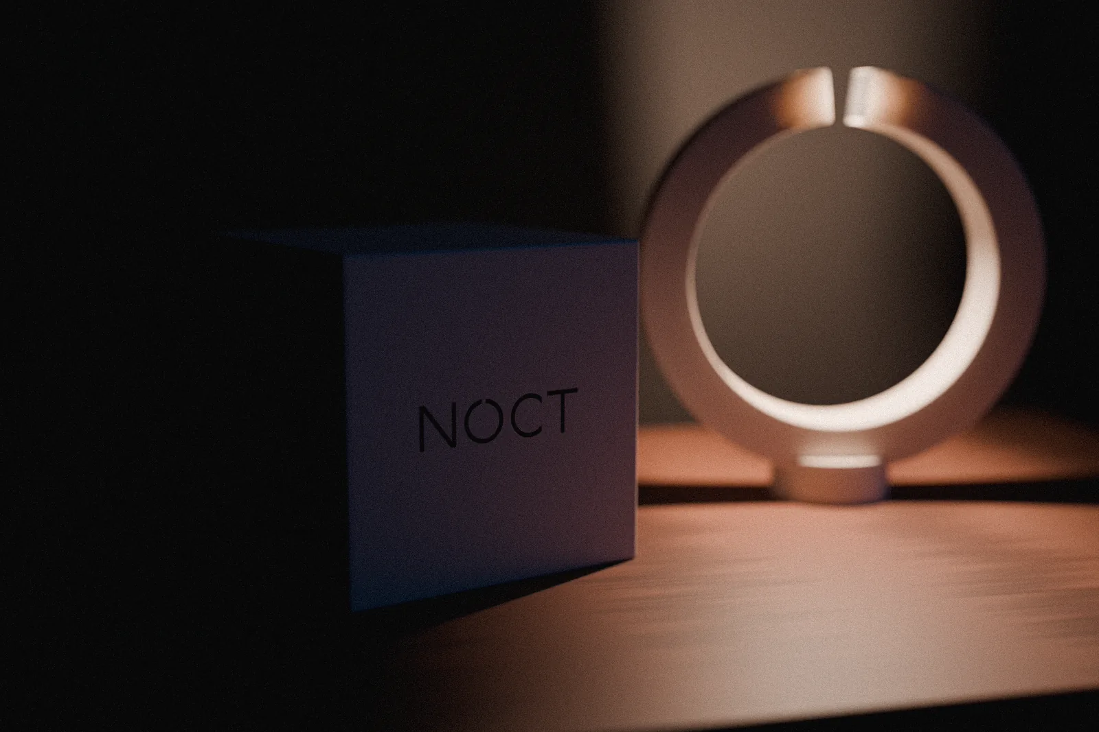 A bone-colored box beside the glowing NOCT lamp, the NOCT wordmark printed on its face.